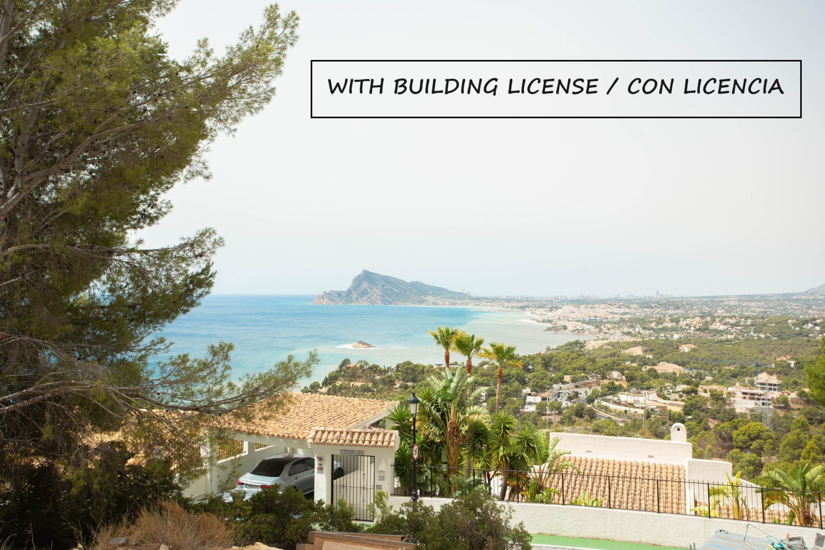 Vue panoramique depuis le terrain sur la baie d'Altea et l'horizon de Benidorm, entourée de pins méditerranéens et de végétation locale.