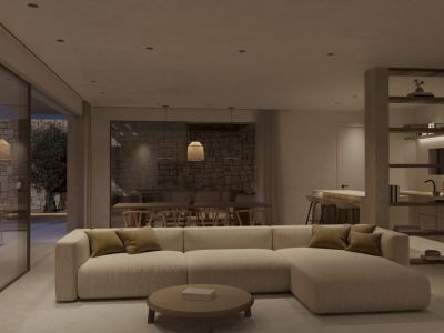 Espace de vie et salle à manger ouverts avec canapé modulaire, table basse ronde et accès à une terrasse en pierre avec olivier. Cuisine intégrée visible en arrière-plan.