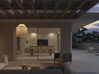 Espace de vie extérieur sous pergola, avec canapés contemporains et luminaire suspendu, s'ouvrant sur une salle à manger intérieure et une vue montagne au crépuscule.