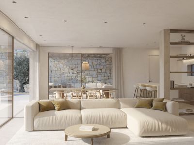 Vaste salon avec canapé sectionnel clair et table basse ronde. De grandes portes vitrées s'ouvrent sur un patio extérieur avec mur en pierre naturelle et olivier.