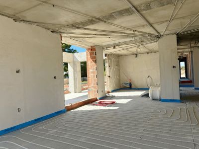 Espace intérieur en construction, présentant l'installation de tuyaux de chauffage au sol sur la dalle de béton. Conduits électriques apparents au plafond brut.