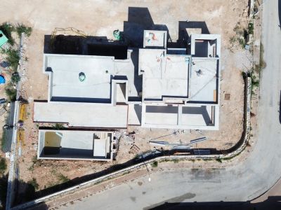 Vue aérienne de la villa en construction, montrant la structure en béton et l'excavation de la piscine privée près de la route.
