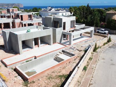 Vue aérienne d'une villa moderne en construction, présentant sa structure en béton et une piscine privée partiellement achevée. Des vues lointaines sur la mer et la montagne sont visibles.