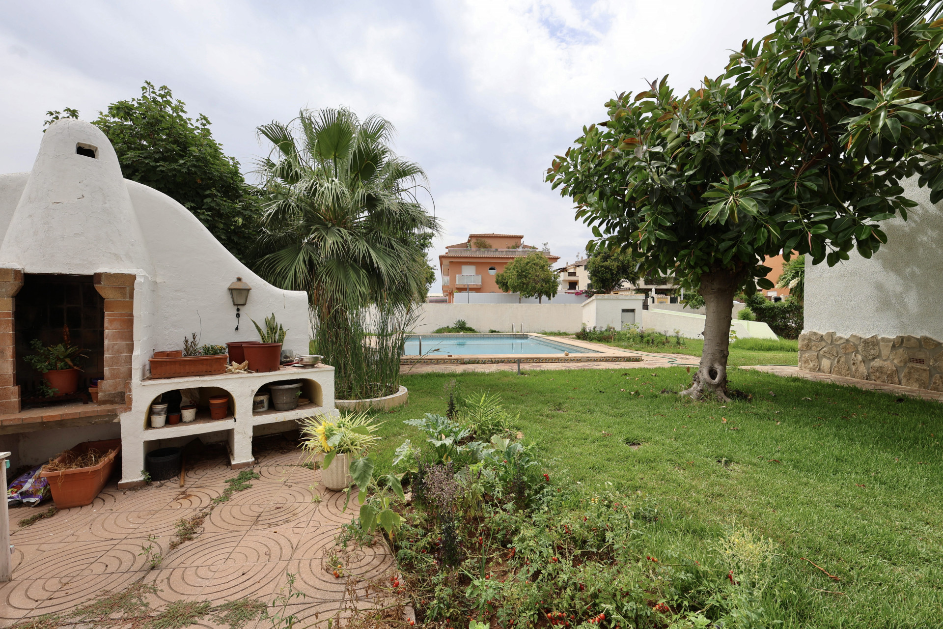 Barbecue intégré avec étagères dans jardin avec piscine et verdure.