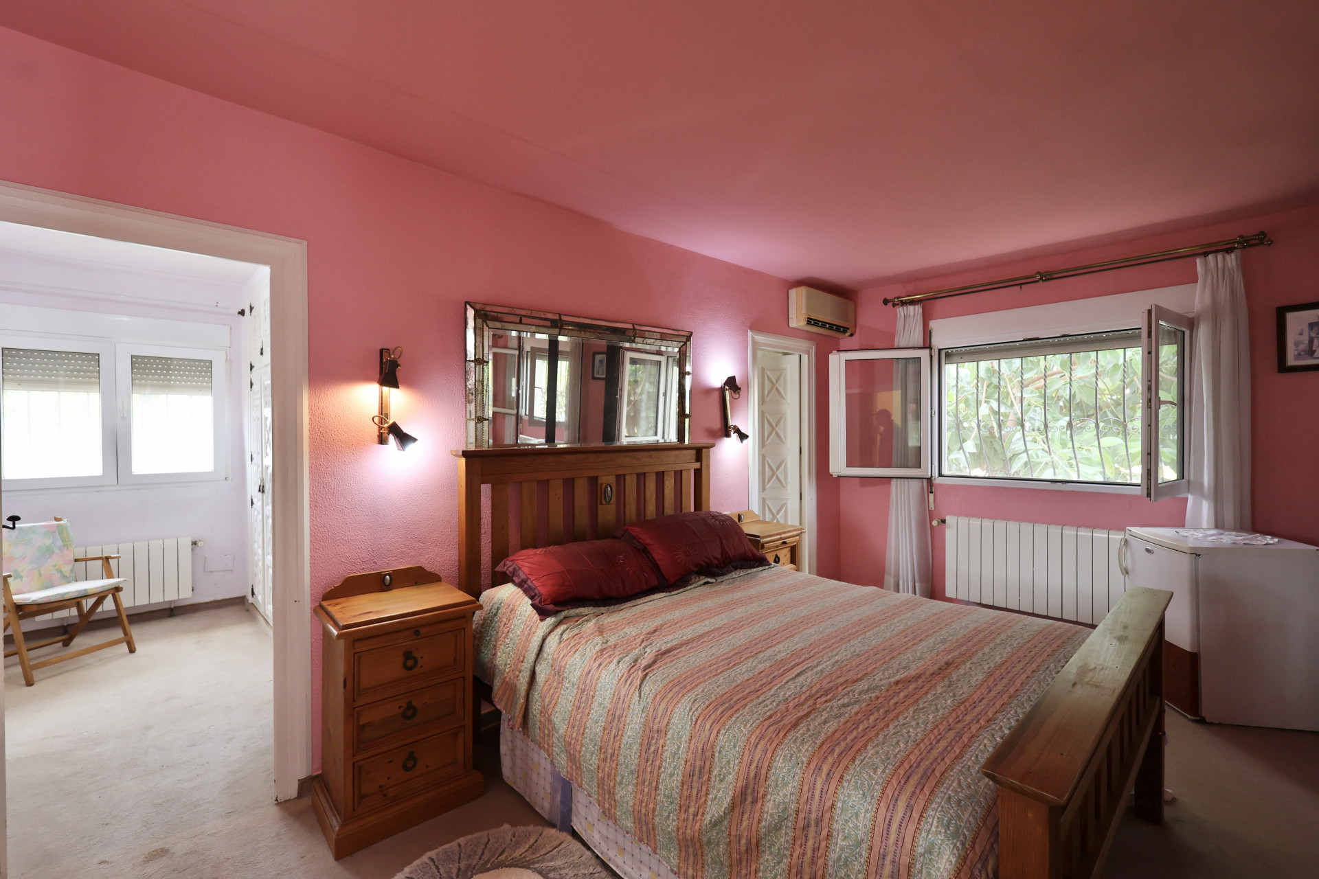Chambre aux murs roses, lit en bois et miroir éclairé par des appliques. À rénover.