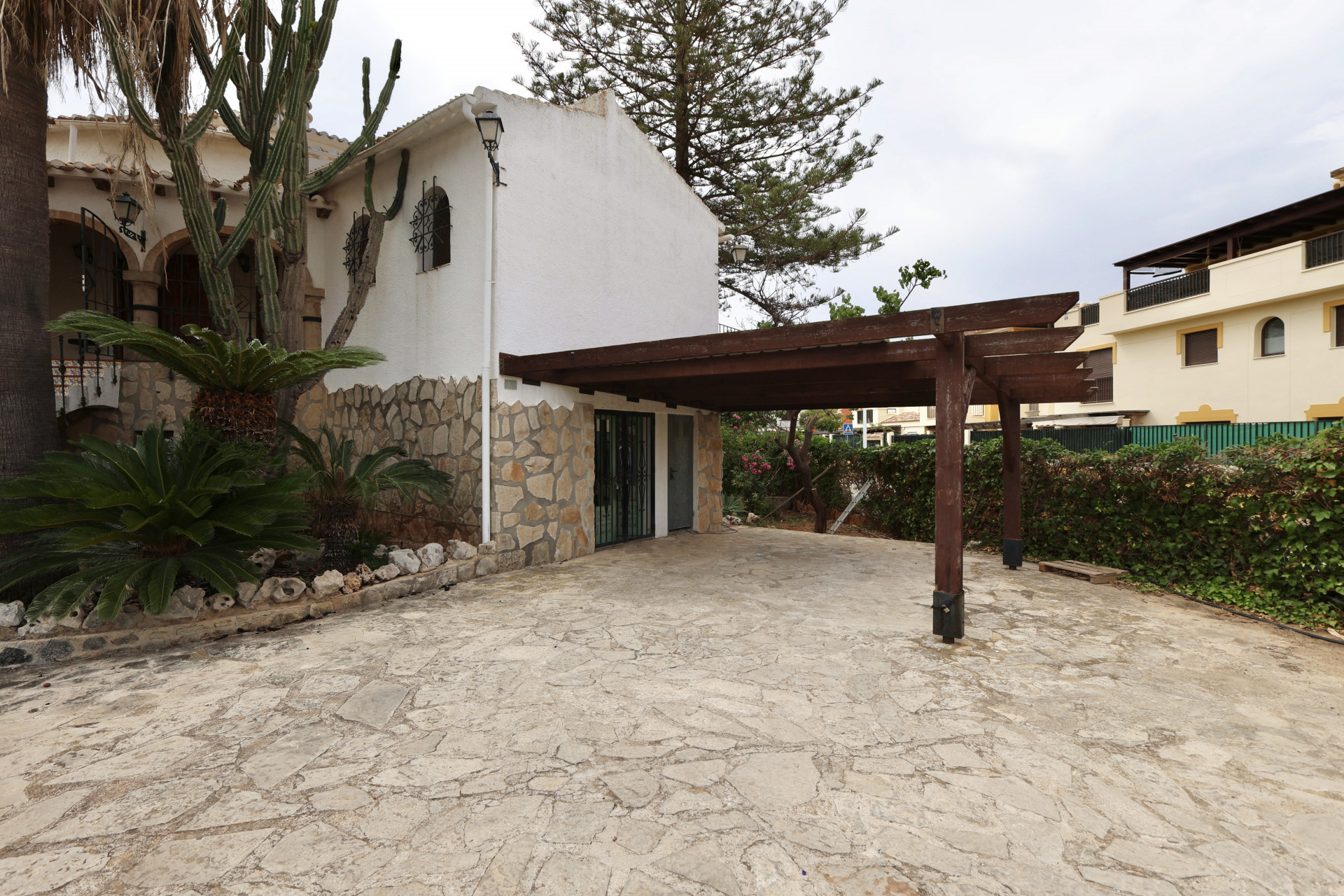 Entrée de villa avec sol en pierre irrégulière et garage couvert avec structure en bois.