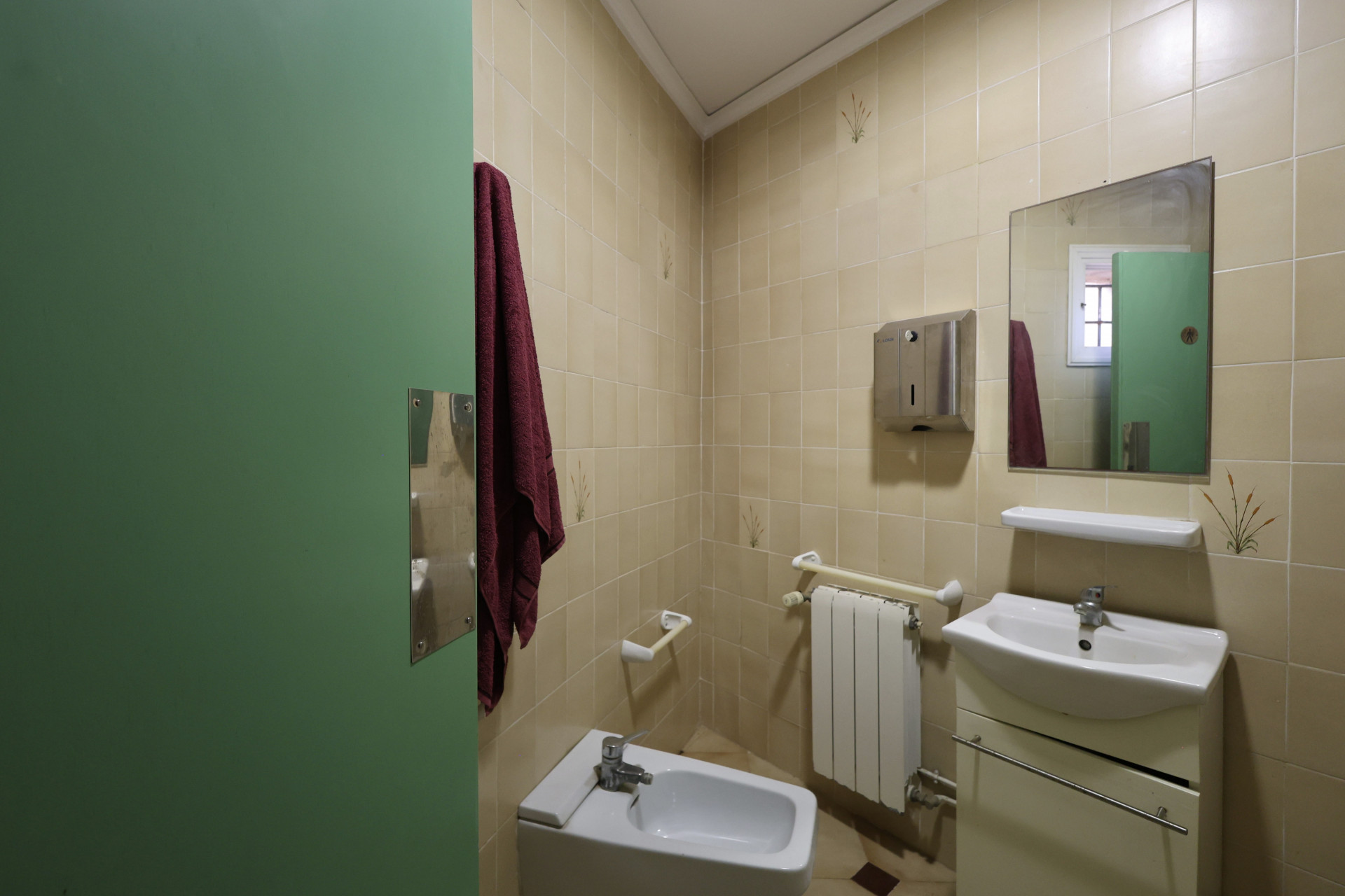 Salle de bain avec carrelage crème, bidet blanc et porte verte.