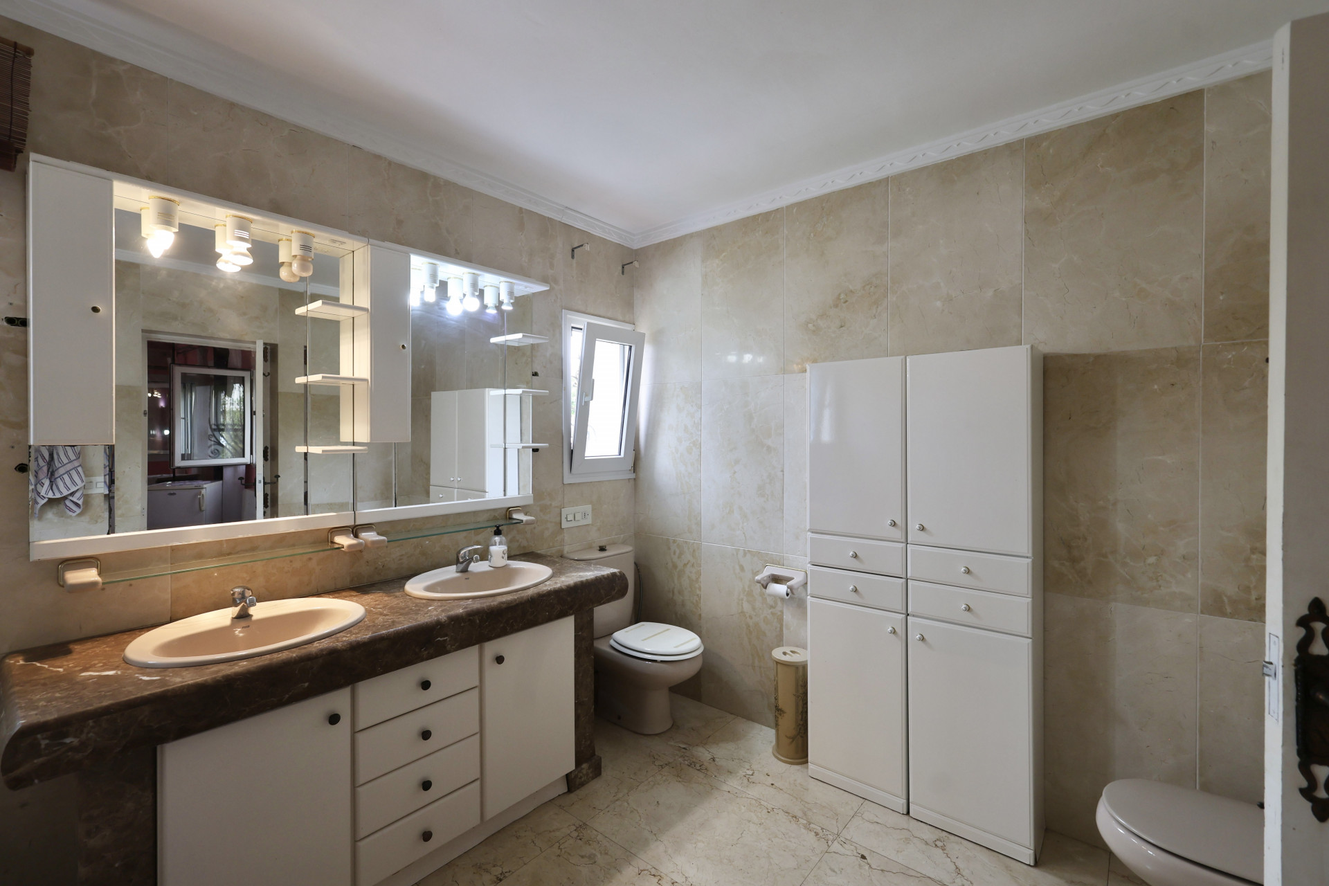 Salle de bain avec double vasque, comptoir en marbre et armoires blanches.