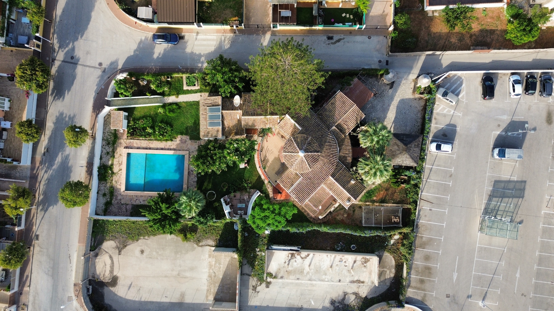 Vue aérienne de la villa avec piscine et toit de tuiles, entourée de verdure et parking adjacent.
