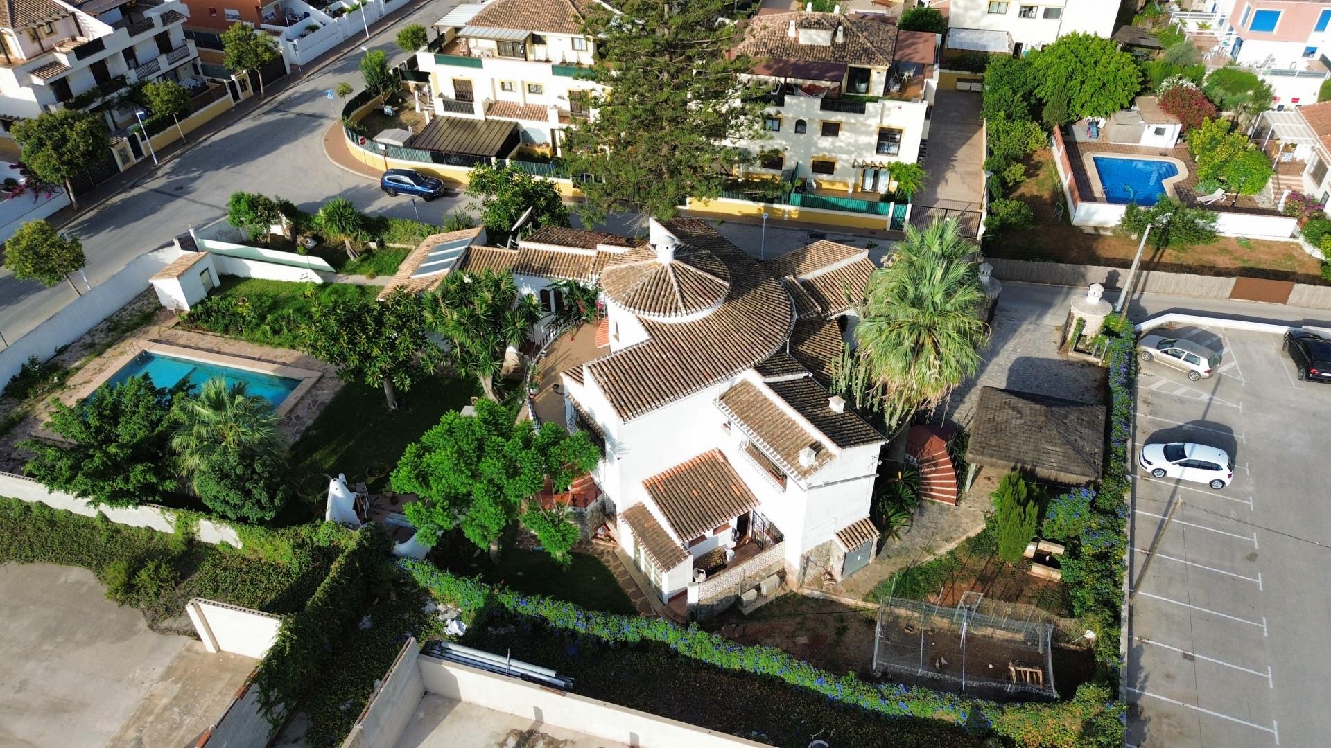 Vue aérienne de la villa avec toit en tuiles, piscine entourée de verdure et parking adjacent.