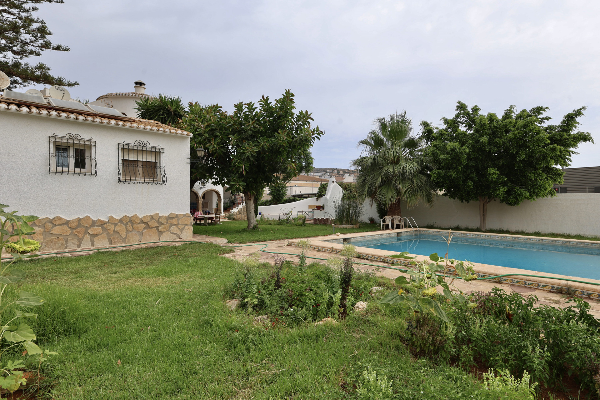 Vue du jardin avec piscine rectangulaire et façade de villa avec détails en pierre.
