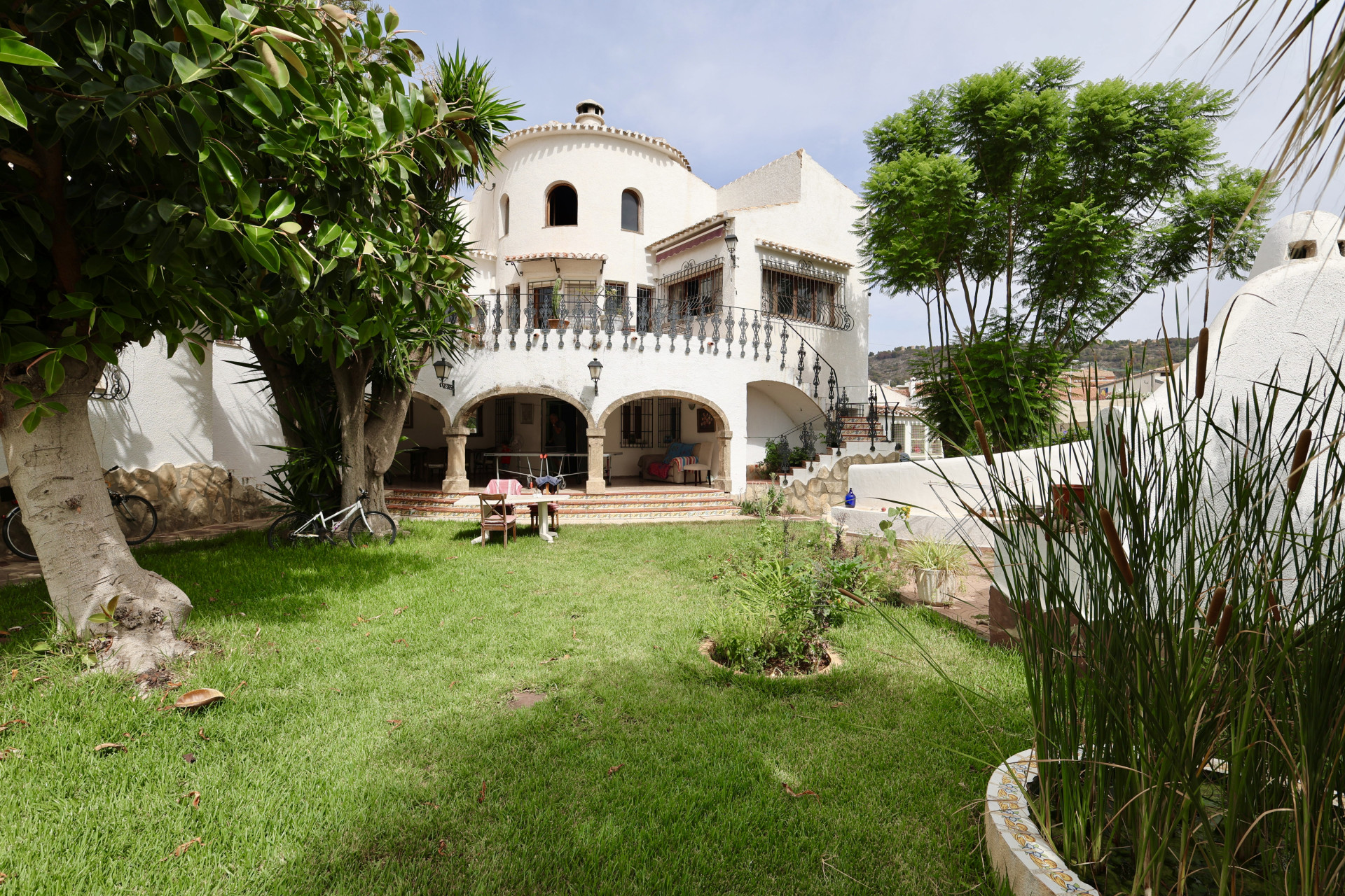 Vue sur la cour avant avec pelouse, verdure et façade blanche de la villa de Javea.