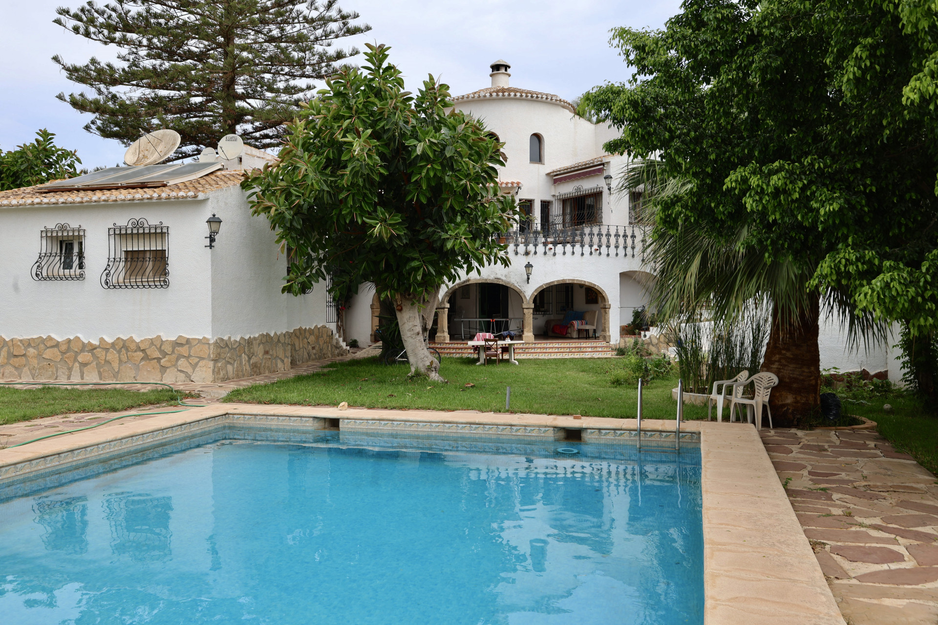 Vue sur la piscine bleu turquoise et la façade blanche de la villa avec détails en pierre et jardin.