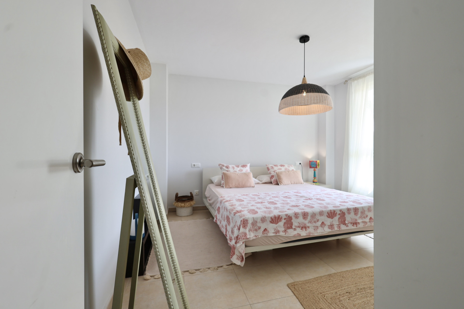 Chambre lumineuse avec lit double, linge de lit à motifs marins et suspension en osier.