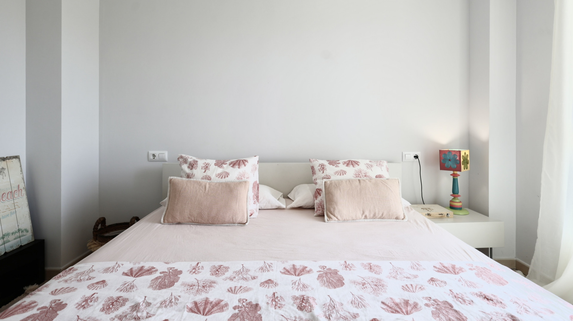 Chambre lumineuse avec lit double, linge de lit à motifs marins et table de chevet blanche avec lampe décorative.