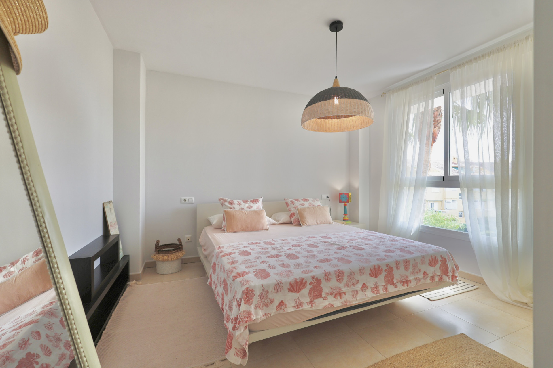 Chambre lumineuse avec lit double, literie à motifs et suspension en osier.
