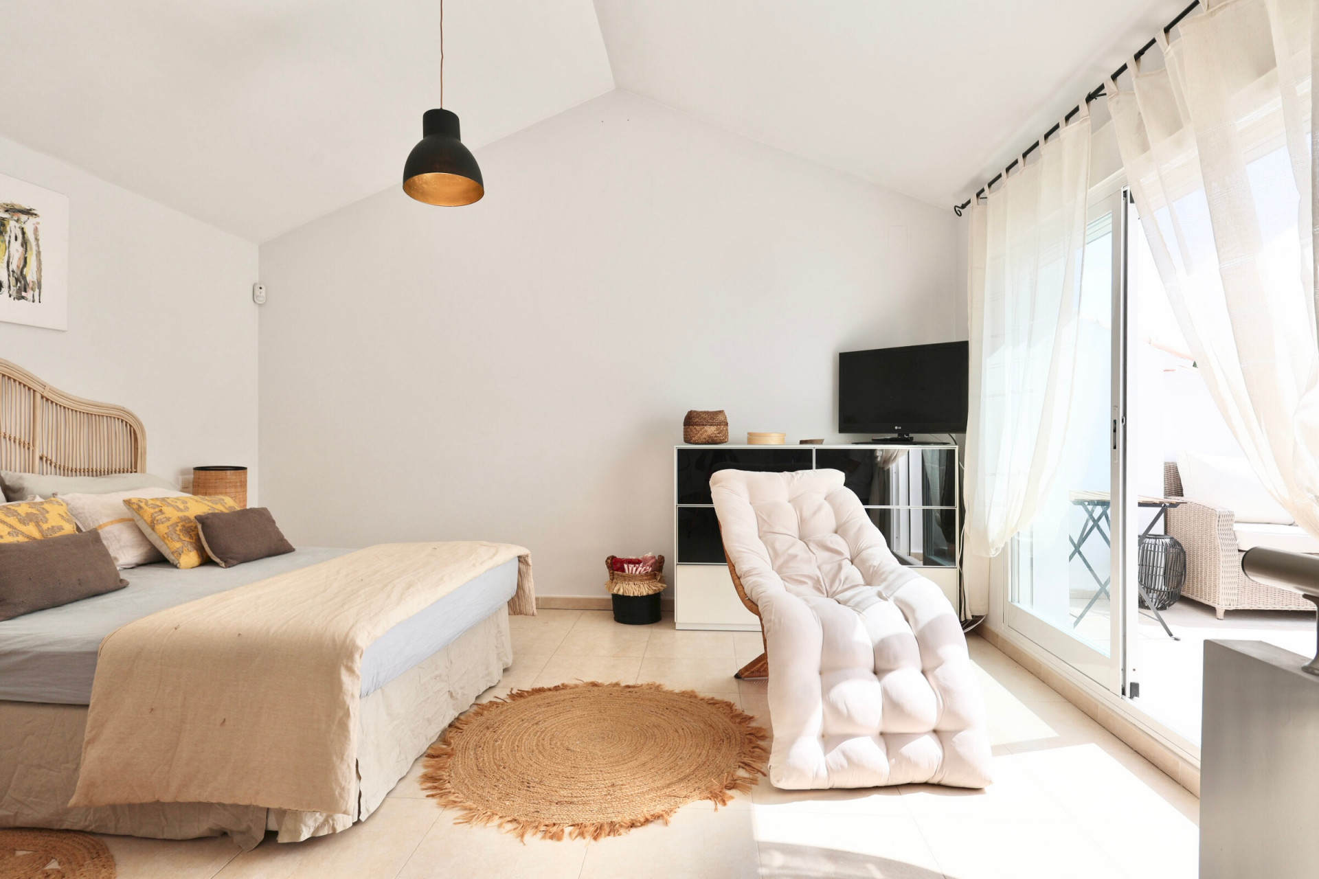 Chambre lumineuse avec lit en rotin, tapis en jute et accès à la terrasse.