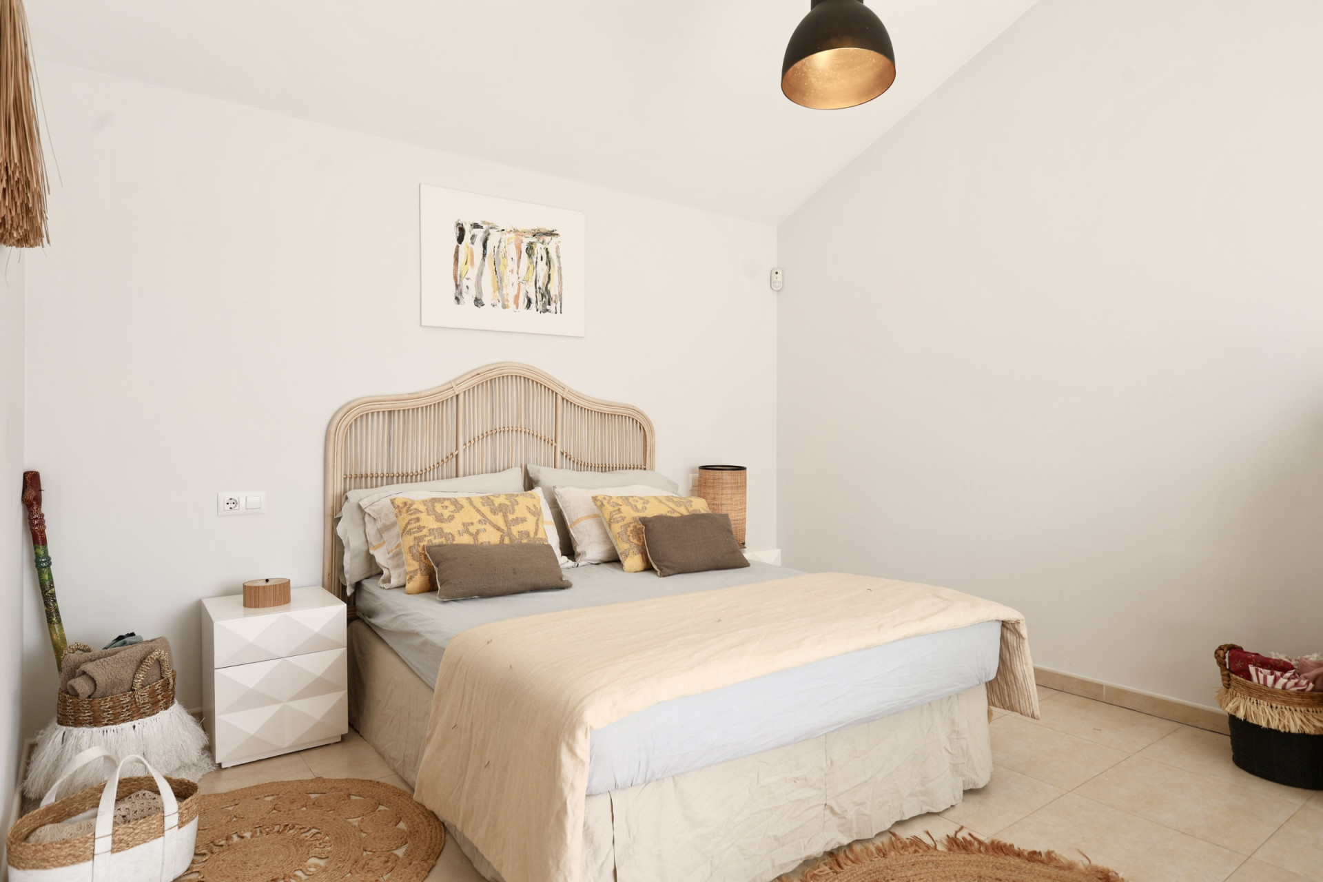Chambre lumineuse avec lit en rotin, tapis rond en jute et décoration minimaliste.