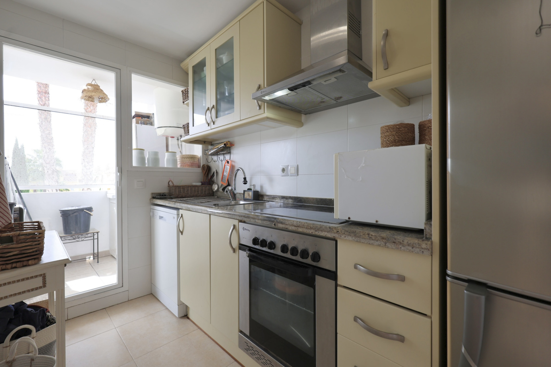 Cuisine lumineuse avec comptoirs en granit, appareils en acier inoxydable et accès au balcon.