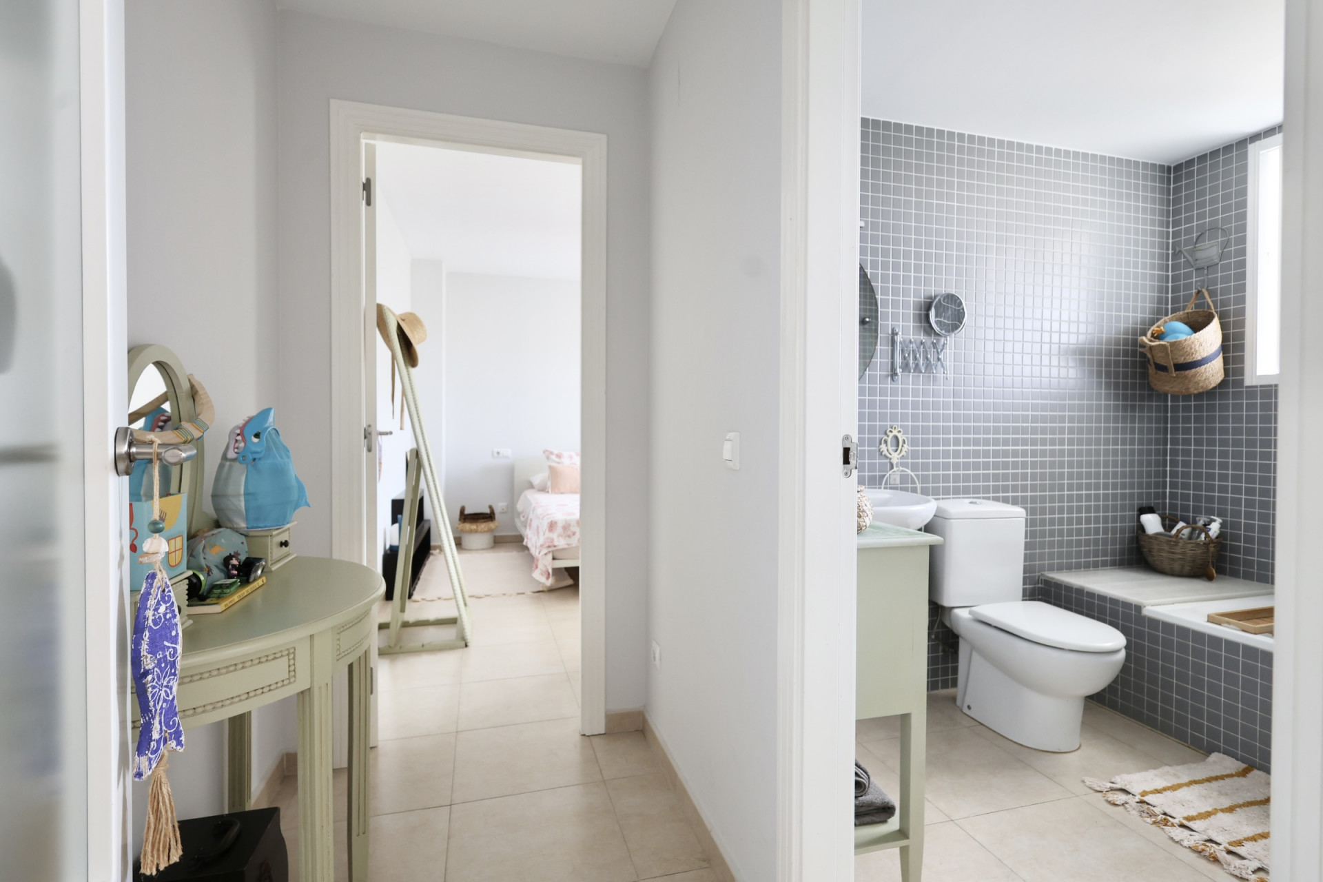 Détail du couloir avec console décorative et vue sur la salle de bain carrelée de gris et la chambre au fond.