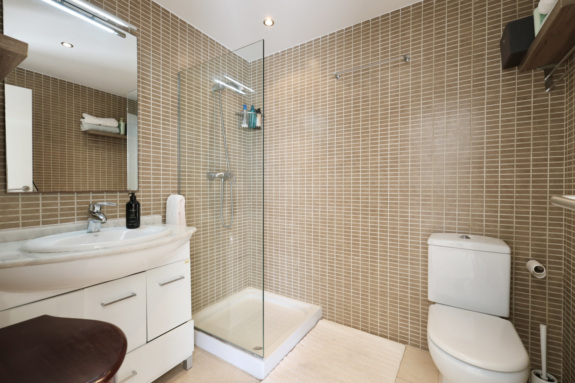 Salle de bain avec murs carrelés couleur sable, douche à l'italienne en verre et lavabo avec comptoir en marbre.