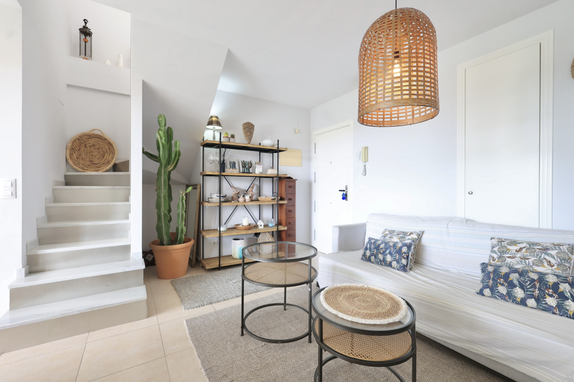 Salon lumineux avec escalier d'accès au duplex, décor minimaliste et suspension en osier.