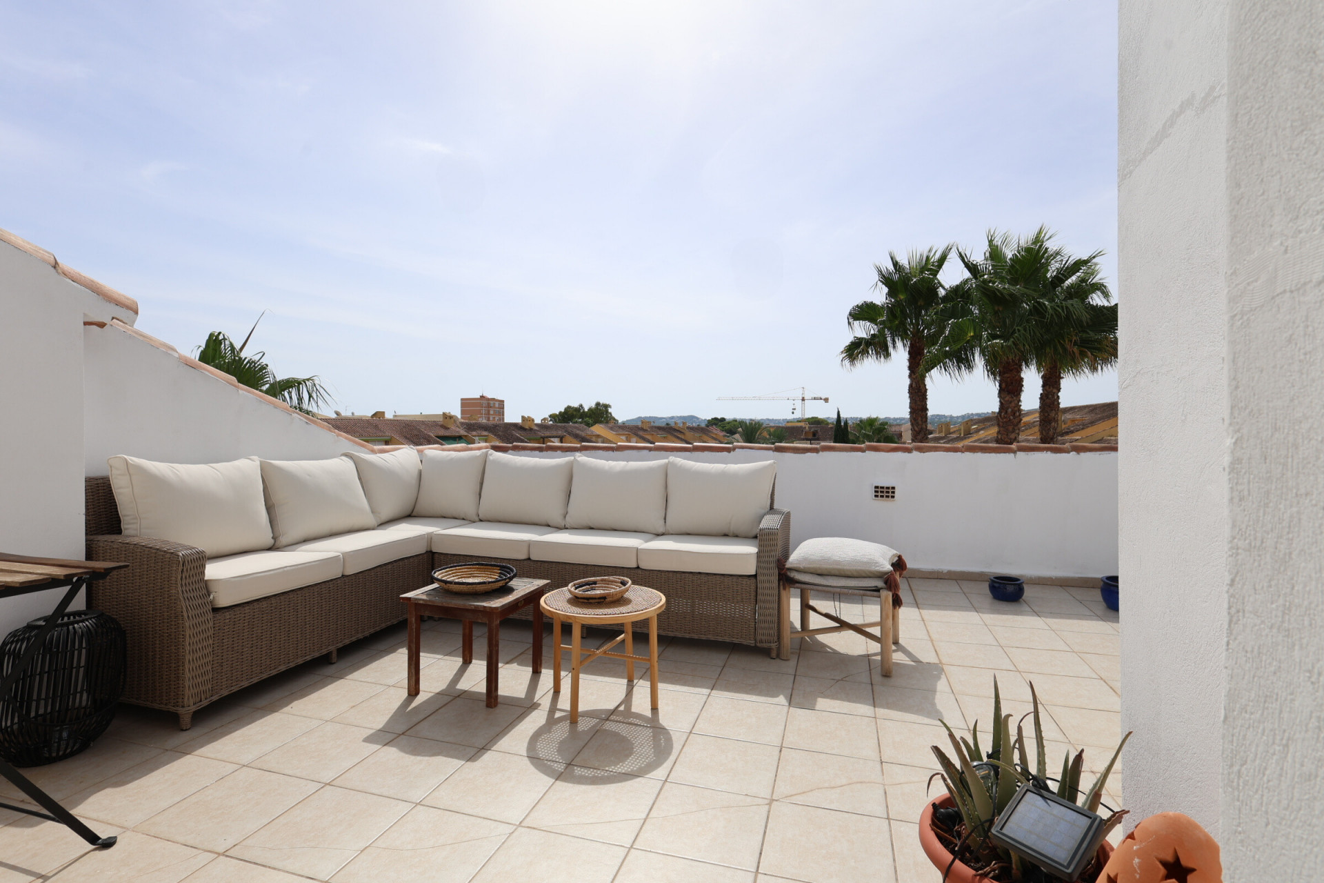 Terrasse carrelée ensoleillée avec canapé d'angle en osier et vue sur les palmiers.