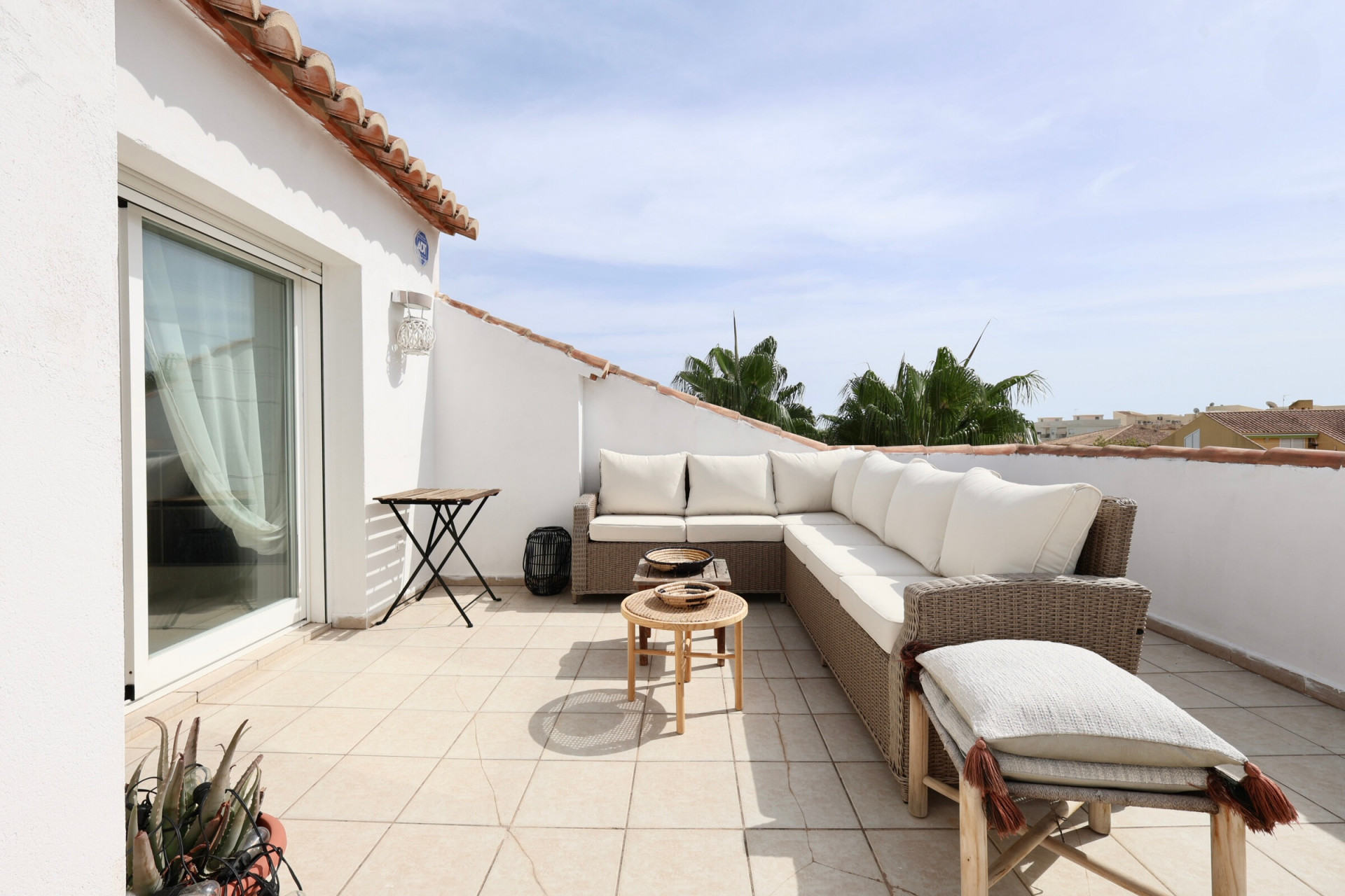 Terrasse ensoleillée avec mobilier en rotin et vue partielle sur l'horizon.
