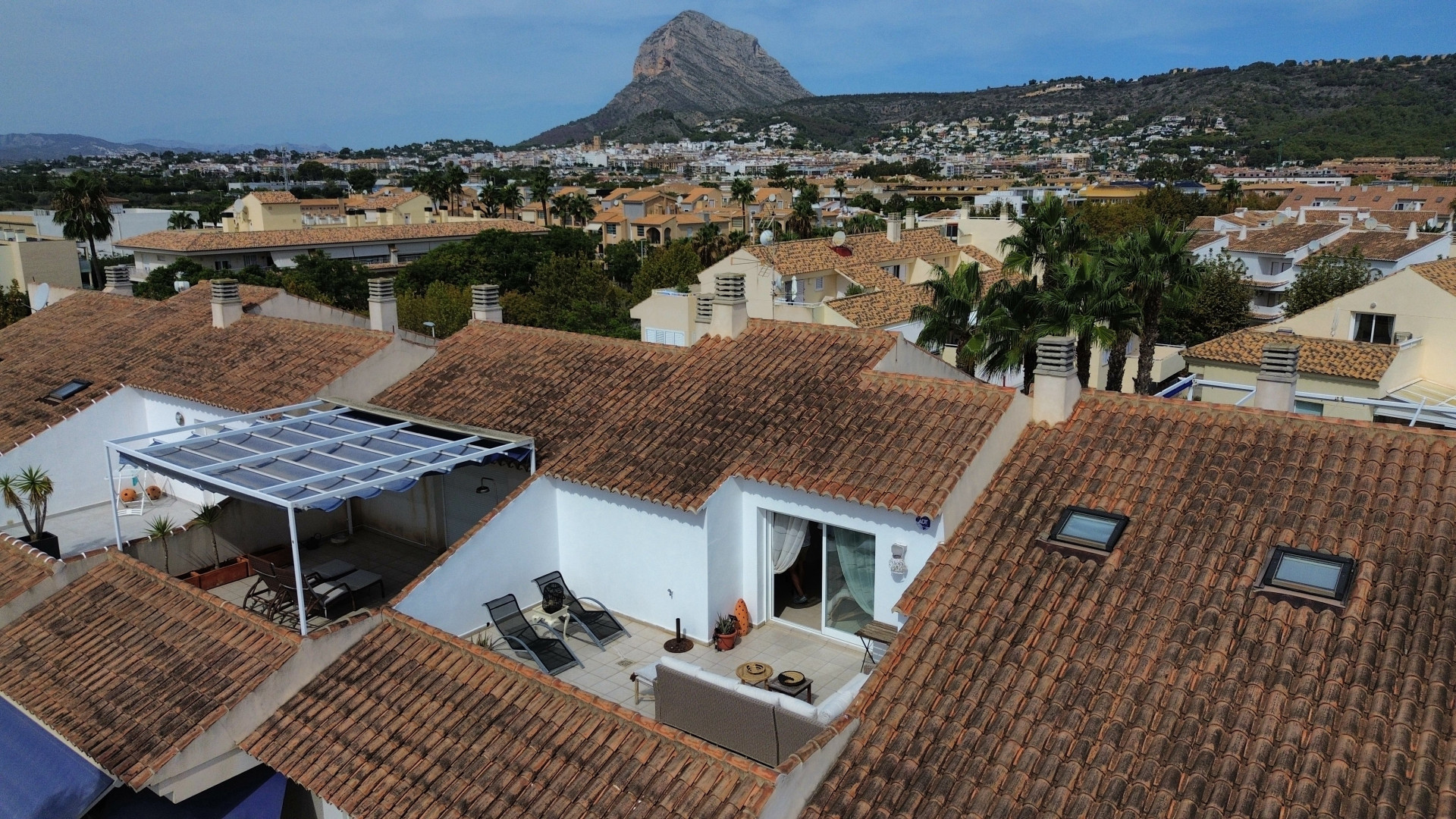 Vue aérienne de la terrasse solarium avec auvent et mobilier d'extérieur, entourée de toits en tuiles.