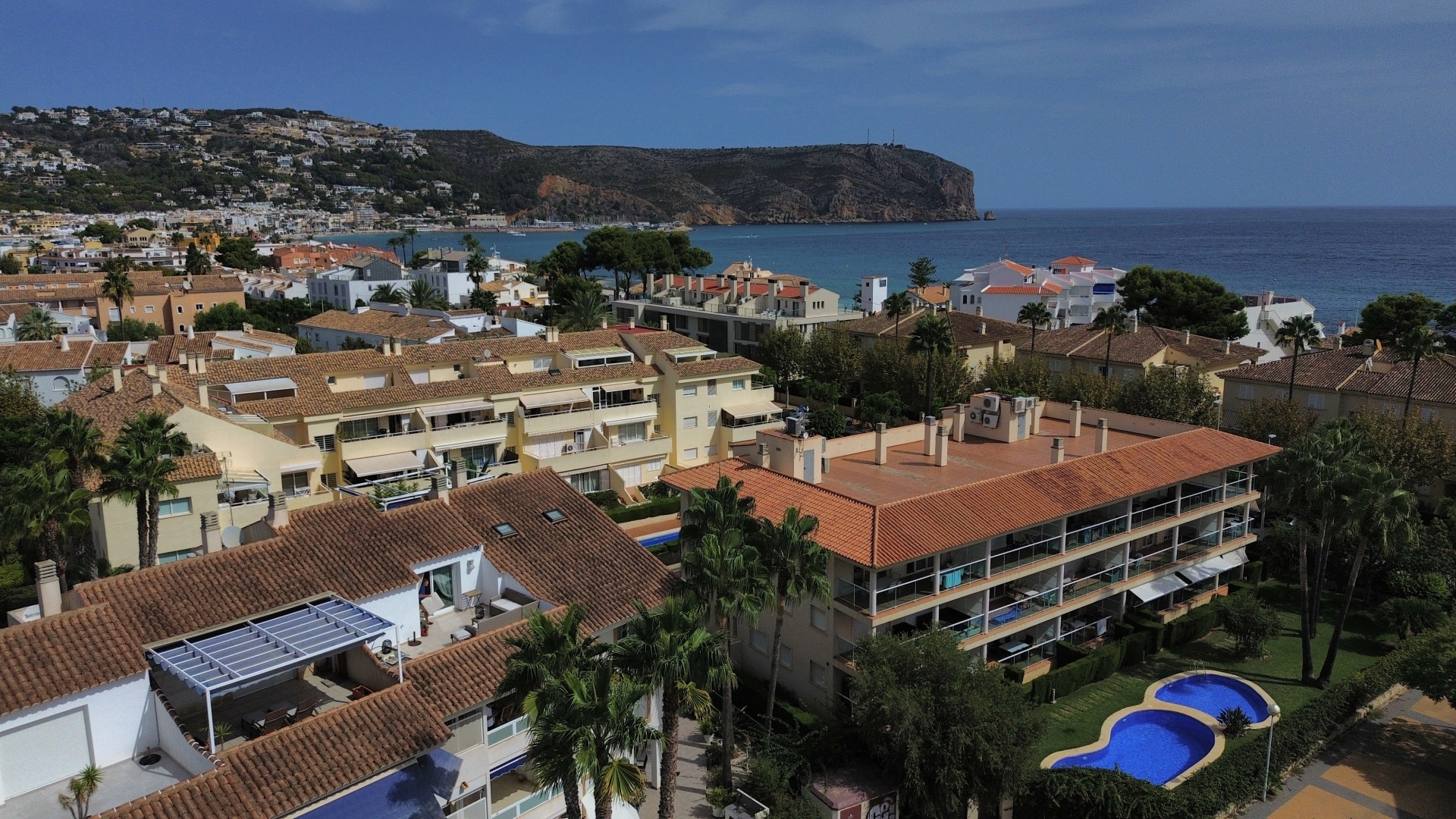 Vue aérienne de l'urbanisation avec piscine et bâtiments résidentiels aux toits rouges près de la côte de Jávea.