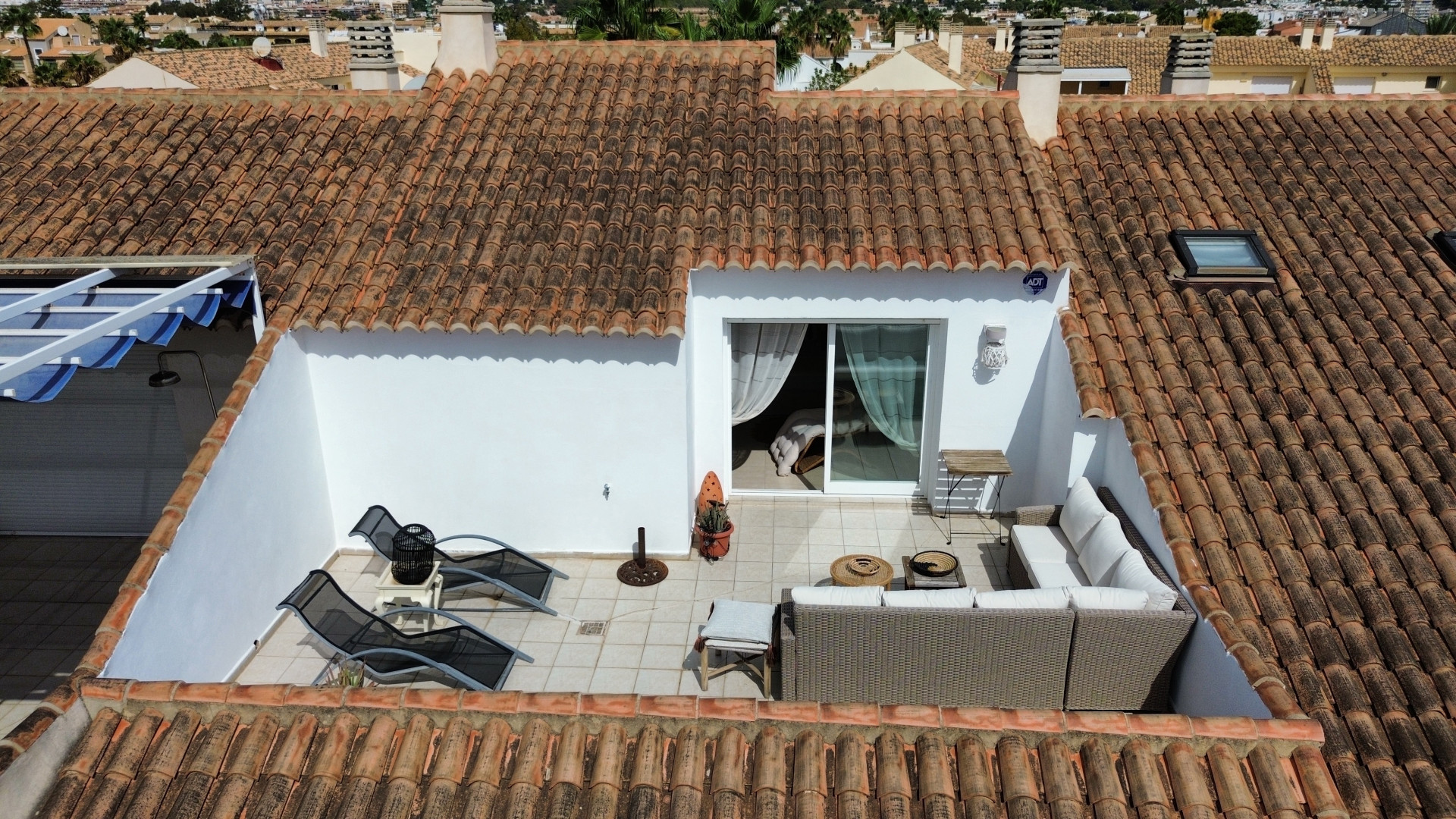 Vue surélevée de la terrasse ensoleillée avec mobilier d'extérieur et accès intérieur.