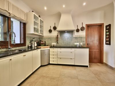 Cuisine équipée avec des armoires blanches de style traditionnel, des plans de travail sombres et un carrelage mural vert. Fenêtre en bois avec store romain et porte en bois massif.
