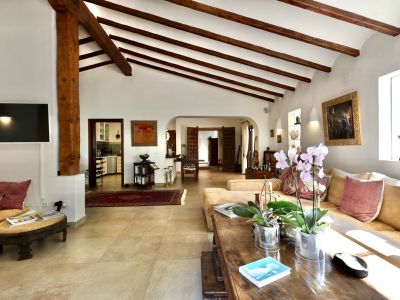 Grand salon avec plafond voûté et poutres en bois foncé apparentes, pilier central, carrelage clair et ouvertures vers d'autres pièces.