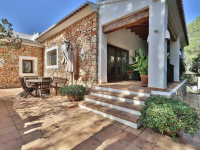Patio extérieur avec murs en pierre naturelle et sol en terre cuite, comprenant un coin repas extérieur et un porche couvert avec poutres en bois.