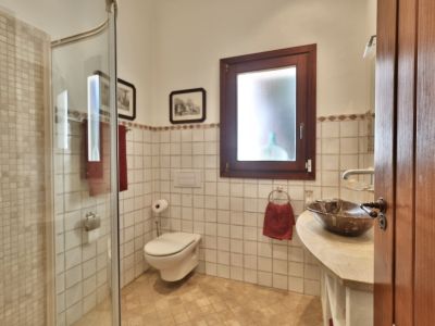 Salle de bain avec douche carrelée de mosaïque, WC suspendu et lavabo en pierre. Fenêtre en bois sombre, carrelage mural blanc et bordure décorative.
