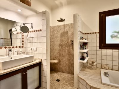 Salle de bain avec lavabo rectangulaire sur meuble en bois foncé et plan de travail en pierre claire. Douche à l'italienne en mosaïque beige et baignoire encastrée. Fenêtre dépolie.