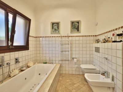 Salle de bain principale avec baignoire balnéo intégrée, fenêtre bois à verre dépoli et carrelage blanc rehaussé d'une frise décorative terreuse.