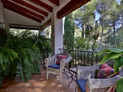 Terrasse couverte avec sol en terre cuite, poutres apparentes et mobilier en osier. Entourée de végétation luxuriante, elle donne sur une forêt dense.