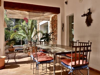 Terrasse couverte avec un ensemble de salle à manger en fer forgé et table à motifs, sur un sol carrelé en terre cuite. Vue sur un jardin méditerranéen luxuriant et un mur en pierre.
