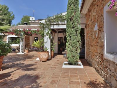 Terrasse extérieure avec carrelage en terre cuite, mur en pierre naturelle et pergola ornée de bougainvilliers, entourée de plantes en pot et d'un cyprès.
