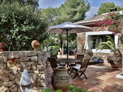 Terrasse extérieure en terre cuite avec ensemble de repas en bois sous parasol, bordée d'un mur en pierre et de végétation méditerranéenne luxuriante.
