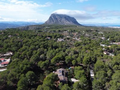 Vue aérienne de la villa intégrée dans une forêt de pins luxuriante, avec le Montgó et la côte de Jávea en arrière-plan.