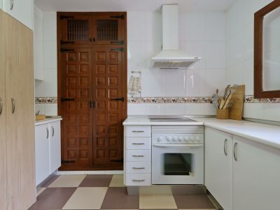 Cuisine fonctionnelle avec four intégré, hotte aspirante et murs carrelés blancs. Un grand placard en bois à portes moulurées et ferrures traditionnelles domine un sol à carreaux.