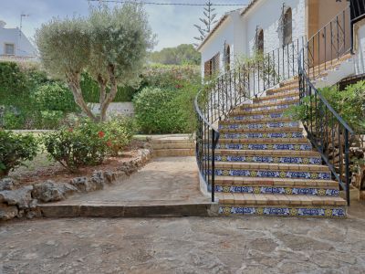 Escalier extérieur en briques avec carreaux décoratifs bleus et jaunes, balustrade en fer forgé, bordé d'un jardin méditerranéen et d'un olivier.