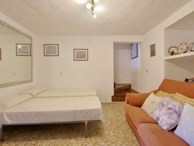 Pièce polyvalente avec deux lits simples, un canapé orange, un sol en terrazzo et des étagères intégrées. Un grand miroir mural agrandit l'espace.