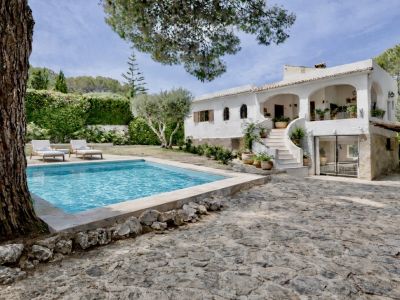 Vue extérieure d'une villa blanche traditionnelle avec piscine privée, patio pavé de pierre et escalier extérieur. Entourée d'un jardin méditerranéen luxuriant.