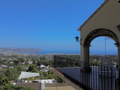 Terrasse couverte avec vue panoramique sur la mer, la ville et le paysage, encadrée par une arche en pierre et balustrade en fer.