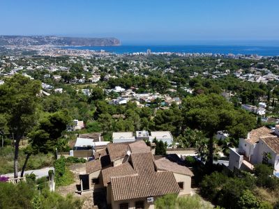 Vue aérienne de Jávea, dévoilant des villas aux toits de tuiles rouges parmi les pins, avec la mer Méditerranée et le Cap de San Antonio à l'horizon.