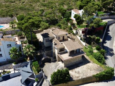 Vue aérienne de la villa à plusieurs niveaux avec toits en tuiles traditionnelles, terrasses multiples et jardins en pente, intégrée à la végétation méditerranéenne.