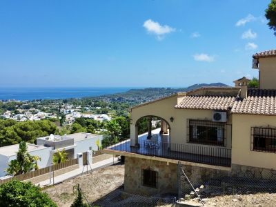 Vue extérieure de la villa avec terrasse couverte, arcades et balustrades noires. La parcelle en pente offre des vues panoramiques sur la mer, la ville et les montagnes.